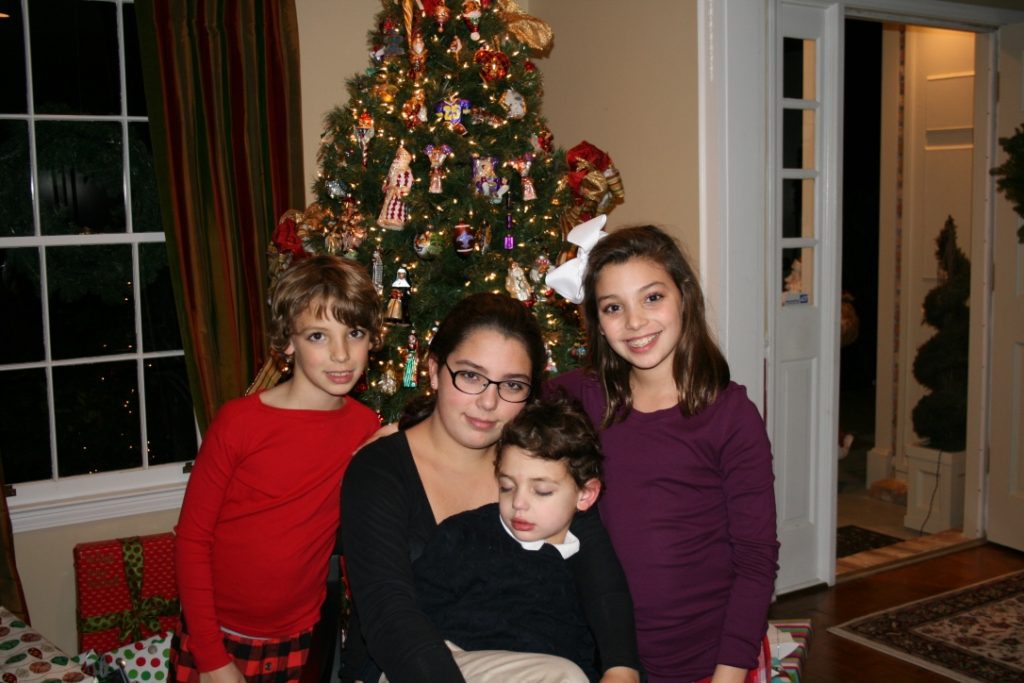 A mom posing in front of a Christmas tree with her two daughters and son