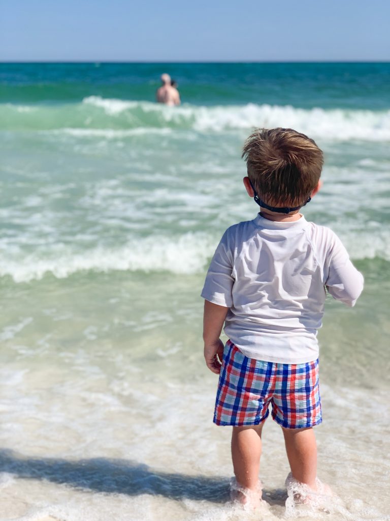 a little boy standing on the beaching looking at the water.