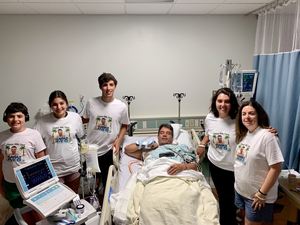 Male patient in a hospital room surrounded by his family after successful surgery while on a family trip to Hawaii