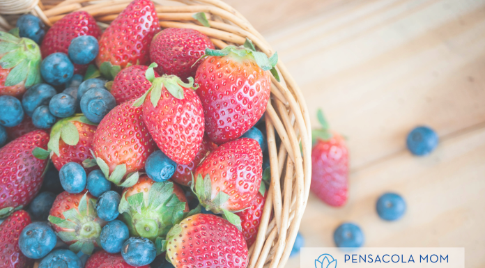 a wicker basket filled with strawberries and blueberries with text "Pensacola Mom Collective Guide to Area Berry Picking"