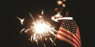 woman's hand holding an american flag with a sparkler in the background