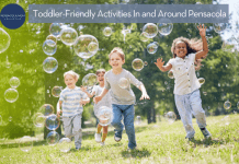 Young children, both boys and girls, running tin the grass with bubbles floating in the air around them.