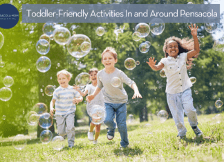Young children, both boys and girls, running tin the grass with bubbles floating in the air around them.