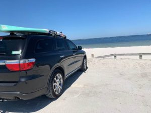 van parked on the beach with a paddle board on the roof