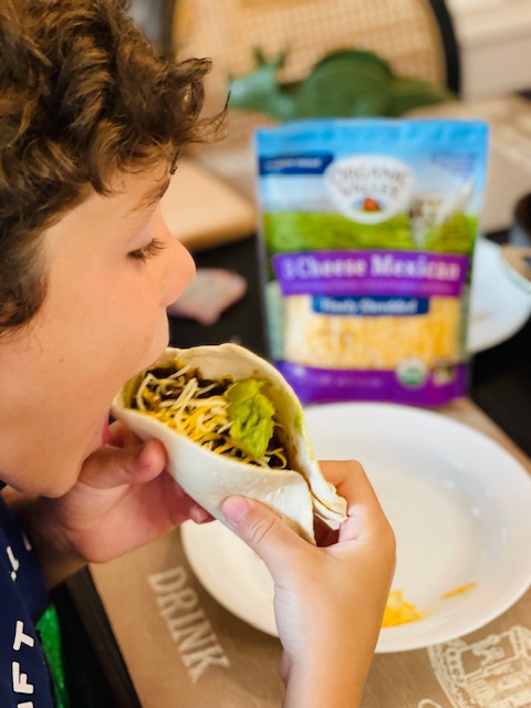 Child eating a taco with Organic Valley Cheese in the background