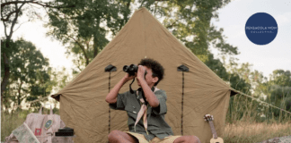 scout in front of tent looking through binoculars