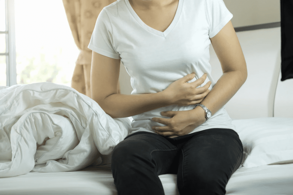 a woman sitting on a bed clutching her stomach