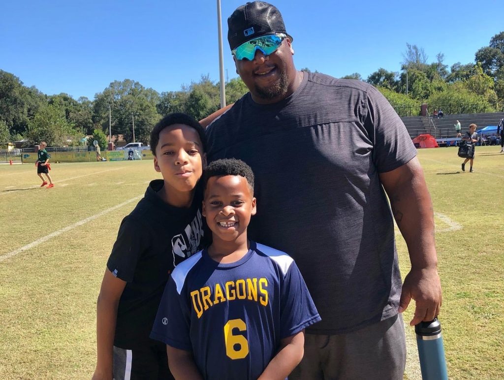 Former NFL player and Pensacola native, Fred Robbins, on the youth flag football field with his two young sons. 