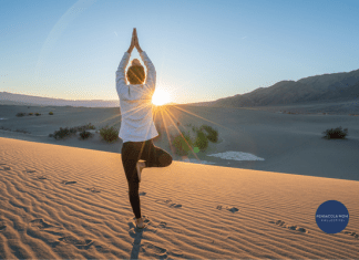 Woman doing yoga tree pose on sand with sunlight shining through.