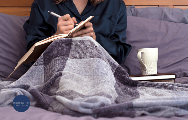 Woman under a blanket with a cup of tea, writing in her Journal