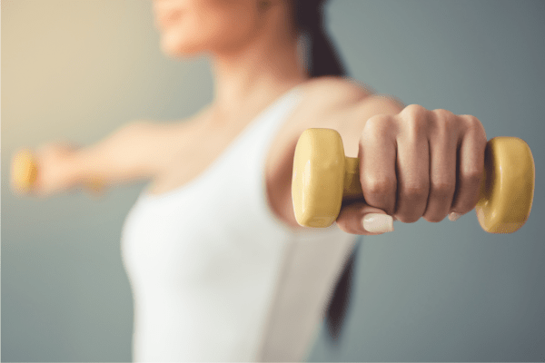 woman holding small yellow hand weights out to her sides.