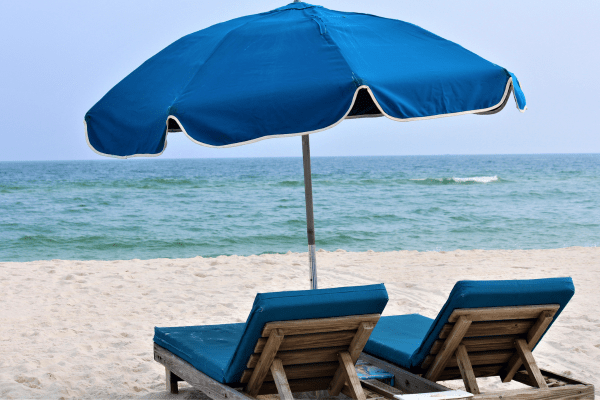 two lounge chairs with a blue umbrella on beach in gulf shores, alabama 