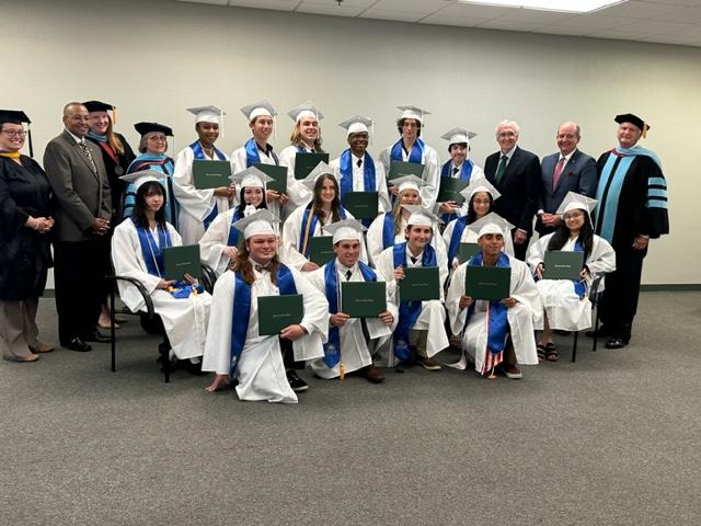 a group photo of the first graduating class of PSC charter academy. Students are in white caps and gowns with blue sashes.