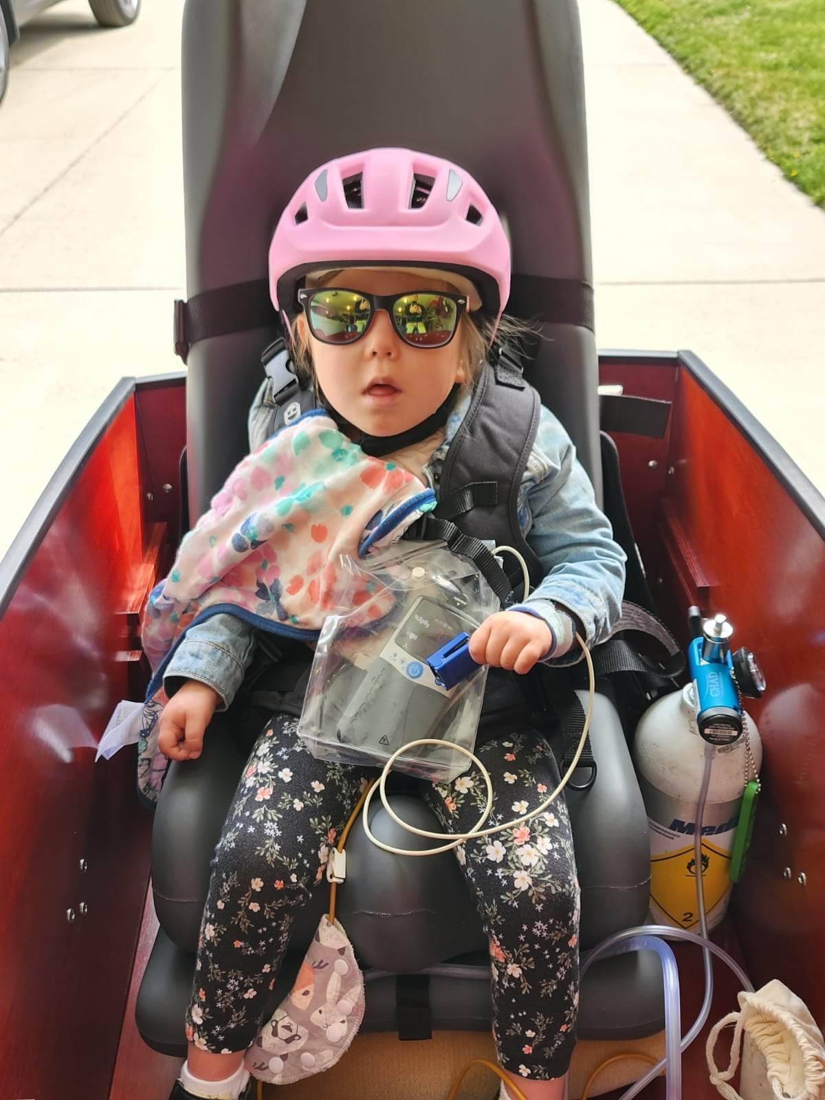 Little girl with medical support equipment and oxygen tank riding in an ebike to school
