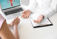 A female doctor and patient talking with only their hands showing. In the background is a computer screen showing the female reproductive system