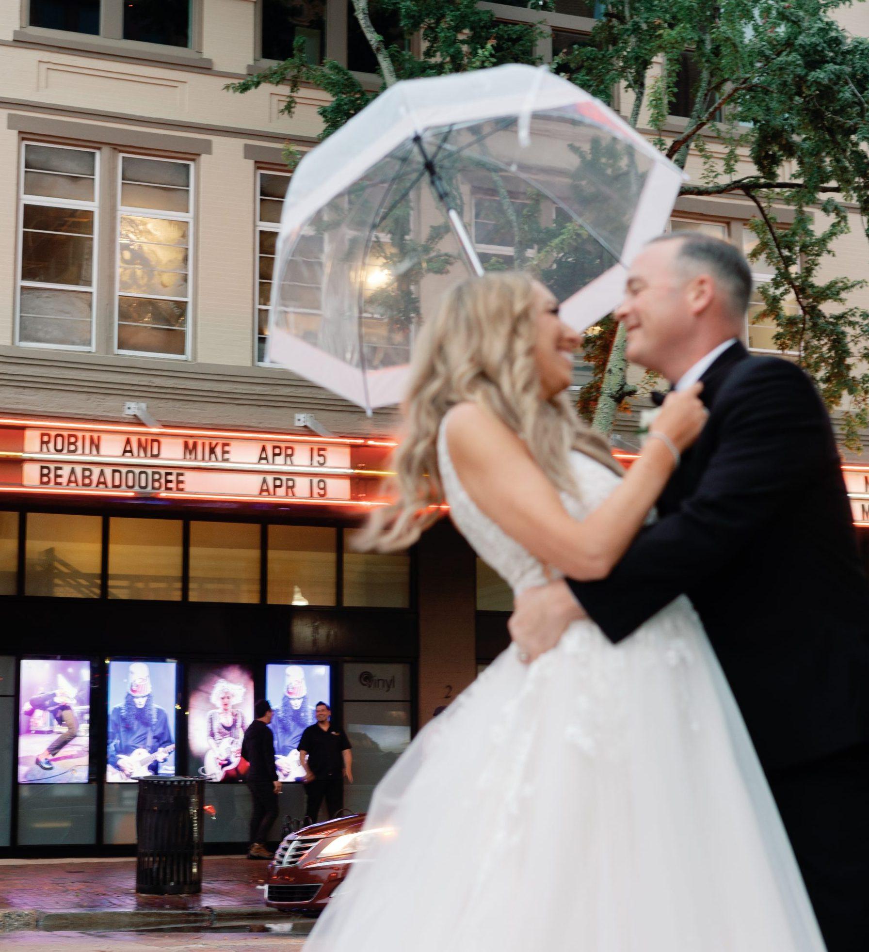 Bride Robin and Groom Mike look lovingly at one another on their wedding day under an umbrella in front of Vinyl Music Hall in Pensacola.