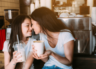 Mom and daughter touching noses. Mom is holding a coffee mug and daughter is holding a smoothie