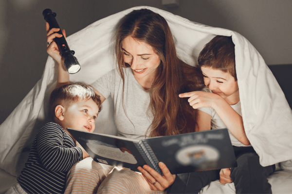 Mom reading to two boys with a flashlight under a blanket