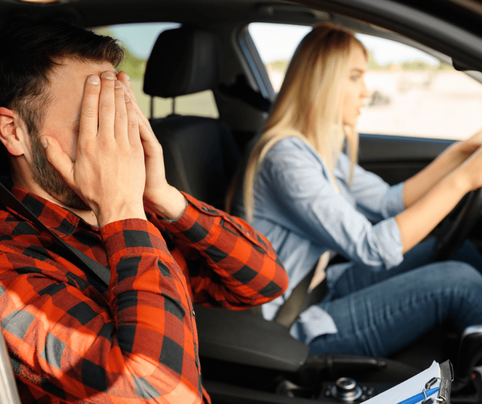 Teenage girl driving with her father who has his hands over his eyes