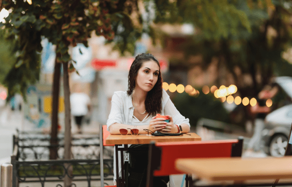 A woman sitting alone at an outdoor table looking sad and lonely