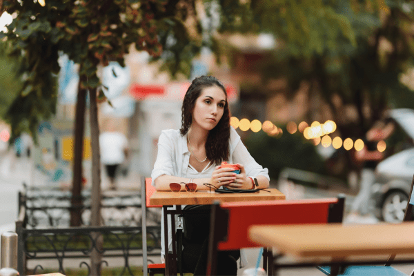 A woman sitting alone at an outdoor table looking sad and lonely