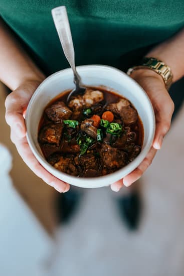 A bowl of beef stew being held by a woman's hands. The photo is taken from above.