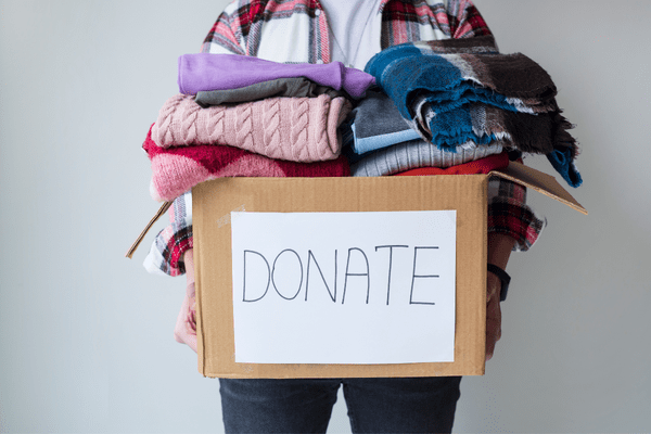 a person holding a box that reads "donate" with clothing items piled on top