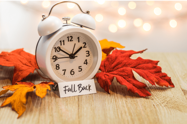 An alarm clock with orange leaves on either side and a sign that says "fall back"