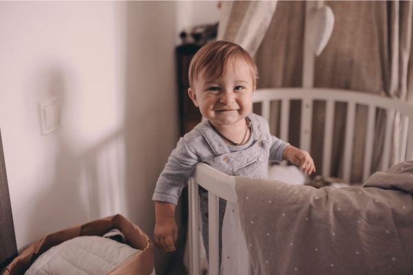 A happy baby standing in his crib in the early morning.