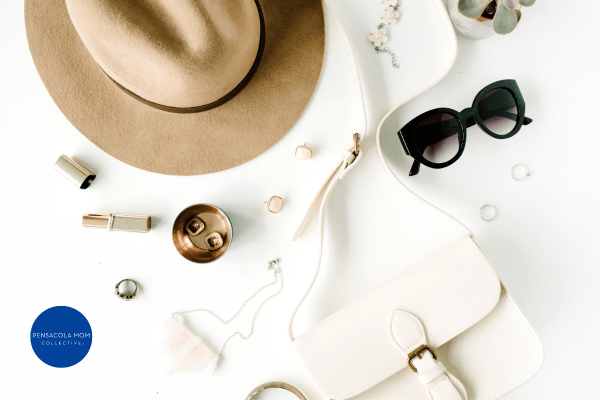 a tan hat, sunglasses, a white purse, and other accessories laid out against a white background
