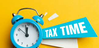 A yellow background with a turquoise colored alarm clock that has a banner reading "tax time"