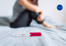 A negative pregnancy test laying on a bed with a sad woman in the background