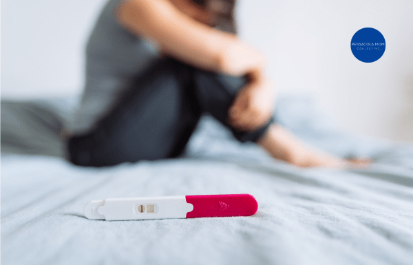A negative pregnancy test laying on a bed with a sad woman in the background
